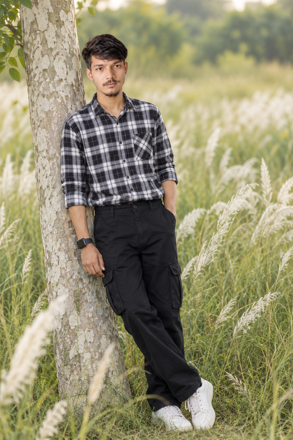 One hand is tucked into his pocket, while the other rests against the tree.